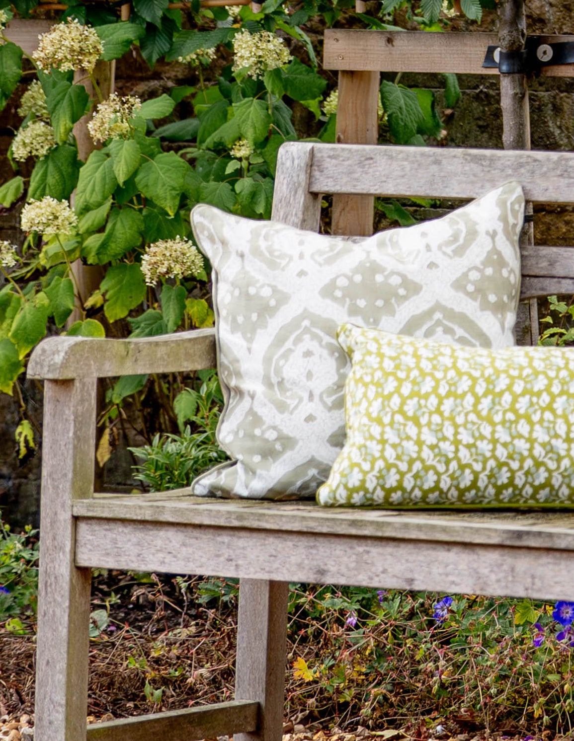Two patterned pillows on a wooden bench in a garden setting.