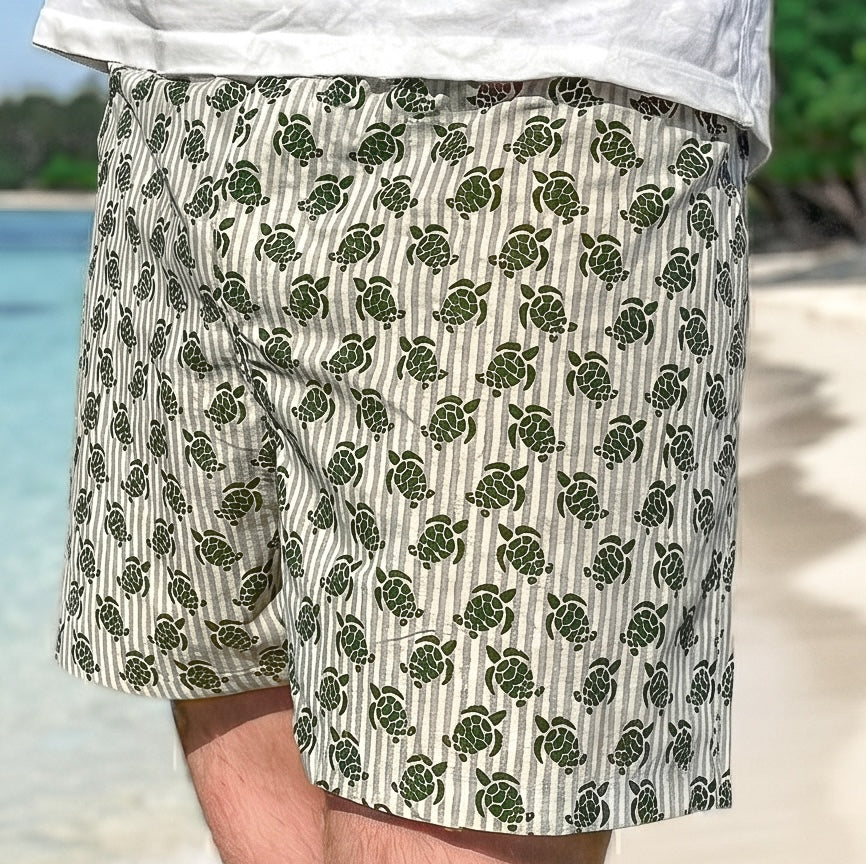 Person wearing shorts with turtle pattern on a beach
